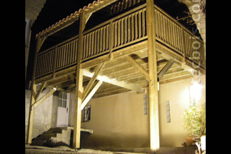 loggia sur balcon en bois soutenu par des poteaux en bois fixés au sol 